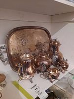 Photo showing complete silver plated coffee and tea set including serving tray, coffee pot, teapot, sugar bowl, creamer, and small bowl with detailed engravings and polished finish.