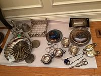 Photo showing assortment of silver-plated serving ware including shell bowls, trays, salt and pepper shakers, condiment holders, honey server, and tongs