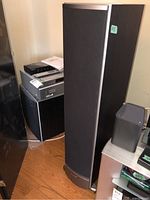 Tall Polk Audio floorstanding speaker with fabric grill and silver trim, positioned next to audio equipment.