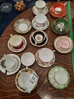 Overview photo showing all 12 teacups and saucers laid out on wood table, displaying variety of colors and floral patterns.