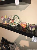 Full view of all five items: two teapots and three matching sugar and cream dispensers, displayed on black shelf.