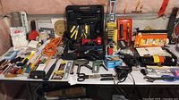 Wide shot of table covered in assorted tools including Black & Decker circular saw, inflators, hammers, staplers, tape applicator, screwdrivers, measuring tape, cable ties and cords.