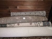 Rolled carpet rugs stacked, showing different colors and patterns including beige and grey tones