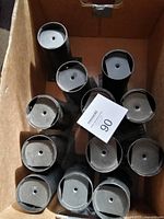 Overhead view of a dozen black metal furniture legs arranged close together in a cardboard box, showing the bottom mounting plates and rounded base caps.