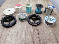 Nine rolls of fishing line, various colors and spool sizes, spread on a wood surface showing condition and labels