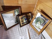 Three framed mirror artworks arranged on fabric, showing an etched duck design, Newcastle Brown Ale branding, and a vintage photo of two girls respectively.