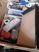 Box filled with assorted men's items, tools, cords, and hardware in various containers