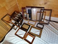 Group of 16 vintage wooden picture frames of varying sizes arranged on a bed.