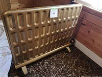 Front angled view of the vintage flat oil radiator showing the flat panel with oval recesses and metallic finish, standing on two legs.