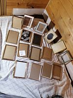 Overview of lot showing 17 vintage mixed metal picture frames in various designs and finishes laid on a fabric surface.