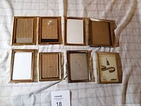 Lot of 8 vintage metal picture frames laid out on fabric surface. Six frames approx 3.5 x 5 inches, one approx 4.5 x 3.5, one approx 5 x 4 inches. Frames vary slightly in gold-tone metal design, some ribbed borders.