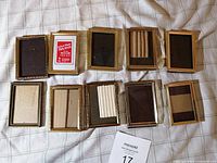 Overview of 10 vintage small metal standing picture frames laid on bed, showing front and back sides