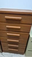 Front view showing six shallow drawers with horizontal wooden handles on a brown painted dresser.