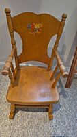 Front view of wooden child's rocking chair with a teddy bear painted on the backrest and turned spindle arms and legs