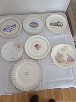 Photo showing seven assorted decorative plates including commemorative, floral, and scenic designs in various sizes and colors.