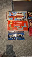 Photo of Uncle Wiggily, Scrabble for Juniors, Deluxe Rummikub games stacked on the floor