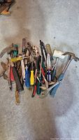 Assorted hand tools laid out on floor showing a variety of hammers, screwdrivers, pliers, and wrenches.