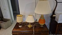 Three assorted table lamps with shades on wooden surface.
