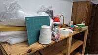 Photo of various sewing and quilting supplies on wooden shelves including batting, thread cone, cutting mat, and baskets.
