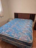 Double bed with a floral blue patterned mattress, wooden headboard with dark stripes