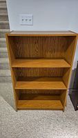 Front view of the bookshelf showing three shelves and wood grain finish