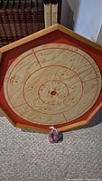Photo showing the octagonal wooden crockanole board with scoring rings and a bag of playing pieces placed in front of it.