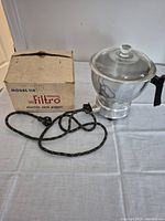 Vintage Filtro electric corn popper, Model 114 shown with original box and fabric covered power cord on white tablecloth.