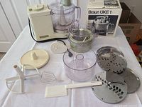 Full lot display showing all components of the Braun UKE 1 food processor including motor base, bowls, multiple discs, mixing blades, spatula, and original juicer box.