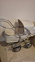 Full size white antique pram angled side view showing chrome frame, wheels and hood