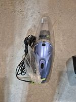 Readyvac handheld vacuum on concrete floor with power cord wrapped beside it, shown plugged cord end in bag.