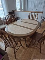 Oval wood frame kitchen table with a beige ceramic tile inset top and four spindle back wooden chairs, arranged around the table