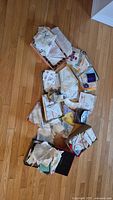Wide view of the assortment of handkerchiefs spread on the hardwood floor, showing multiple boxes with folded items.
