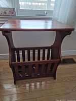 Solid wood magazine rack table shown from one angle, displaying tabletop and magazine storage compartment with vertical slats.