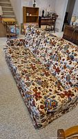 Front view photo of retro floral fabric couch showing tufted back and cushioned seat, upholstery detailed in 1980s-style floral pattern