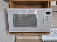 Front view of Panasonic white microwave oven with closed door showing keypad and LED display.