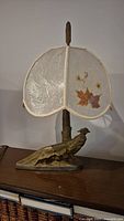 Full view of the lamp showing metal pheasant base, tree trunk body of lamp, and vintage scalloped lampshade with pressed leaf designs.
