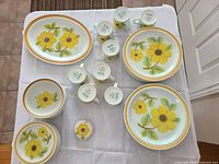 Overview of all pieces laid out on table with platter at top left, plates, bowls, mugs and sugar bowl arranged