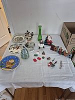 Table setup displaying assorted seasonal decorative items including plates, glassware, and holiday figurines and ornaments.