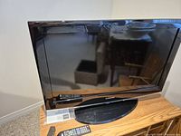 Samsung 31-inch TV on wooden table with remote on the base of the TV.