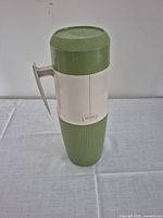 Closed vintage Thermos bottle in olive green and cream colors with handle.