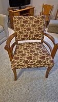 Front view of the wood frame chair showing floral fabric upholstery and curved wooden armrests.