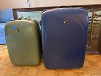 Front view of two Heys hardcase suitcases, one blue and one green, standing side by side on floor.