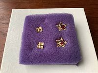 Two sets of vintage 14K gold earrings displayed on a purple foam pad showing floral and star shapes with garnet stones.