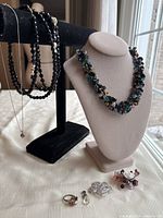 Seven pieces of assorted vintage jewelry including two necklaces on display stands and other pieces arranged on tabletop.