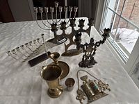 Top-down view showing entire lot arranged on white fabric, including various menorahs, kiddush cups, candle holder, and keychain.