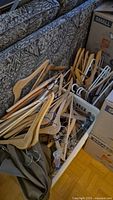Pile of various wooden clothes hangers on floor near patterned couch with cardboard boxes visible.