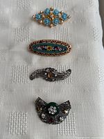 Photo showing all four vintage costume brooches arranged vertically on white textured fabric.