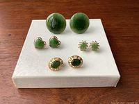 Four pairs of vintage green earrings on a white textured box, showing shapes and designs clearly
