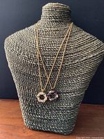 Two vintage pendant necklaces displayed on a woven stand showing full chain length and pendant design.