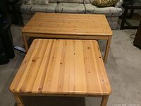 Front view of two pine tables, one square side table in front and one rectangular coffee table behind, showing wood grain and condition.